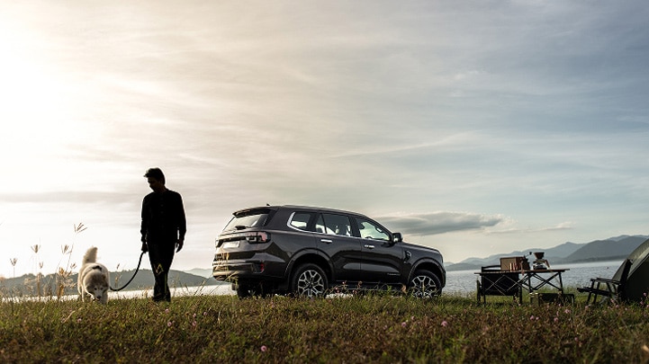 A person walking their dog with a Ford SUV in the background.